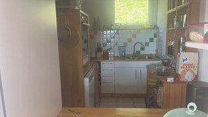 Eine kleine Küche mit weißen Schränken, einem Fenster und verschiedenen Küchengeräten.