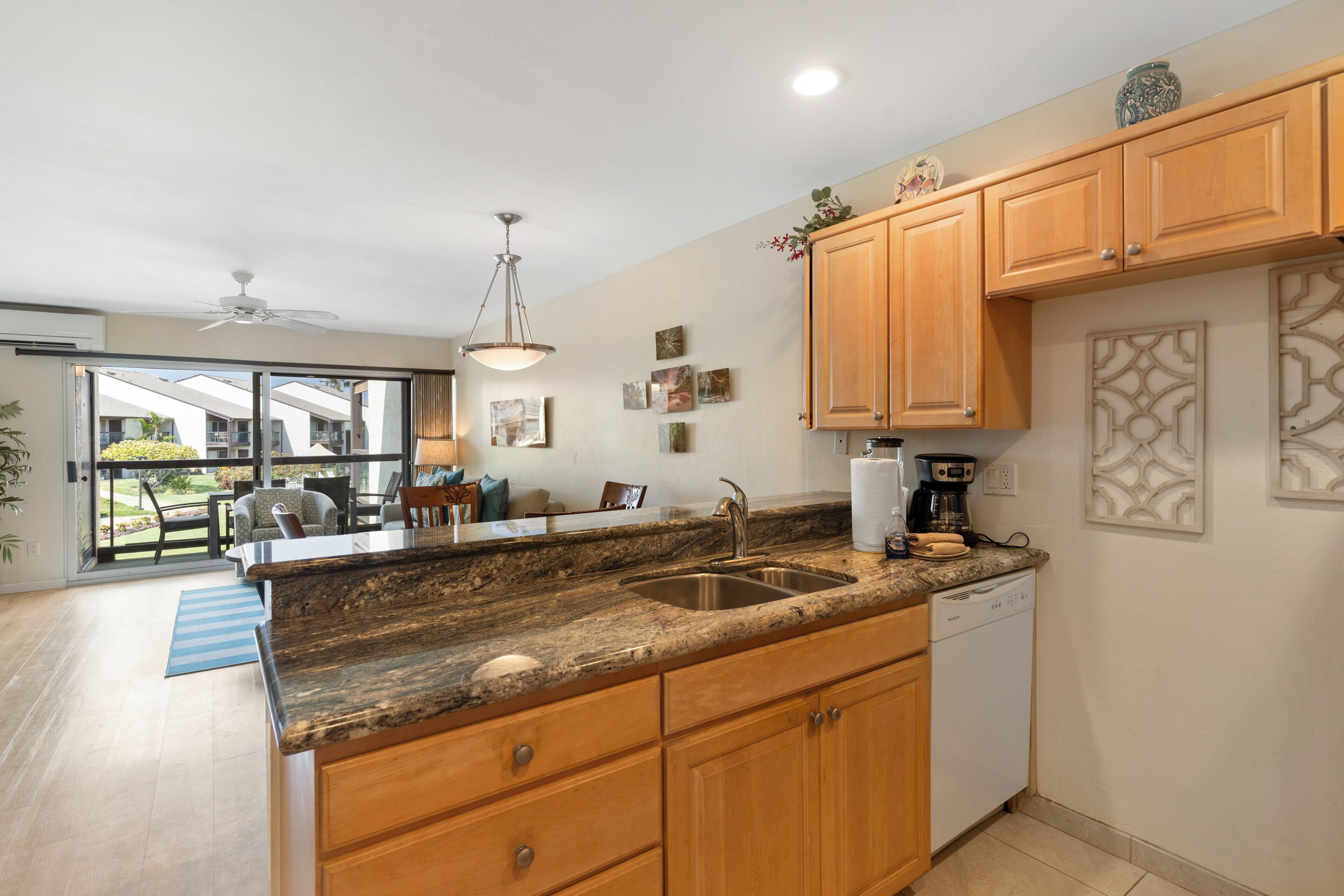 A kitchen with granite countertops, wooden cabinets, a dishwasher, and a coffee maker.