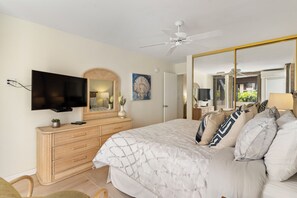 Ein Schlafzimmer mit Bett, Fernseher, Kommode, Spiegel und Deckenventilator.