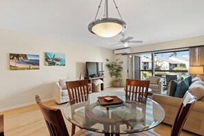 A modern living room with a glass dining table, wooden chairs, a sofa, and a television.