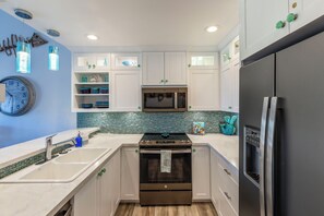 A modern kitchen with white cabinets, a stainless steel refrigerator, a microwave, and a stove.