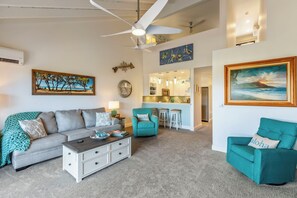 A living room with a sofa, a teal armchair, a coffee table, and a ceiling fan.