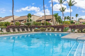 A clear blue pool with lounge chairs and palm trees, surrounded by resort buildings.