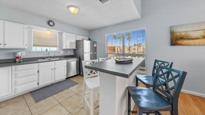 A modern kitchen with white cabinets, a granite countertop, and a breakfast bar with chairs. - 121 E Aries - Angel's Paradise (South Padre Island)