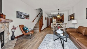 Ein geräumiges Wohnzimmer mit Kamin aus Stein, einer Ledersofa und einem Glastisch, sowie eine Essecke mit einer Chandelier.