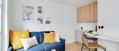 Un salon moderne avec un canapé bleu, une table à manger en bois et un coin cuisine doté de meubles en bois.