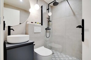 Une salle de bain moderne avec un lavabo, des toilettes et une douche, le tout de couleur blanche.