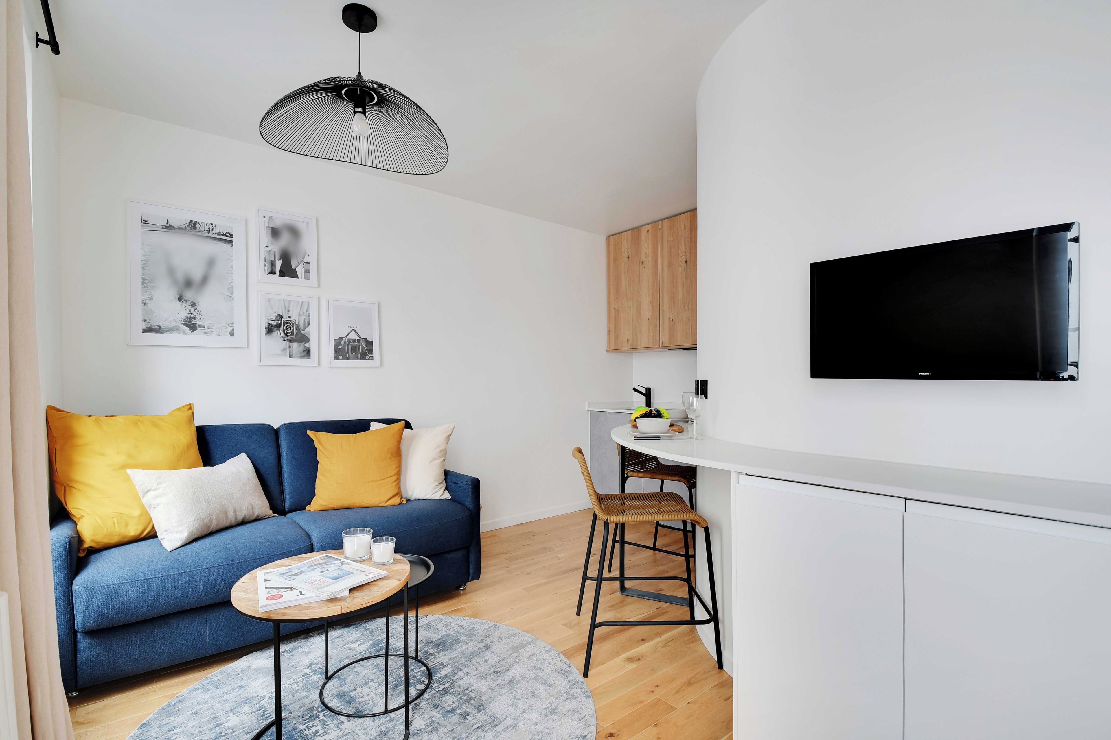 A modern living room with a blue sofa, a round coffee table, and a TV mounted on the wall.