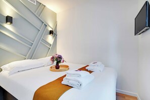 Ein ordentlich bezogenes Bett mit weißen Leinen, ein Holztablett mit einem Blumenstrauß und gestapelten Handtüchern.