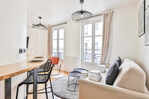 A modern living room with a sofa, a dining table with chairs, a small round table, and a radiator.