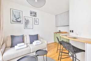 Una sala de estar moderna con un sofá, dos sillones, una mesita y una zona de cocina con mostrador y taburetes.