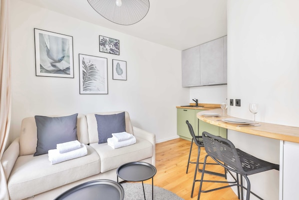 A modern living room with a sofa, two chairs, a small table, and a kitchen area with a counter and stools.