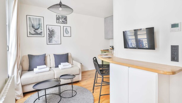Un salon moderne avec un canapé, une petite table ronde et un coin repas comprenant un comptoir en bois et des chaises.