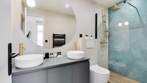 Une salle de bain moderne avec deux lavabos, un grand miroir et une douche.