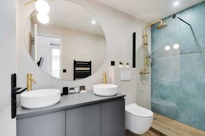 A modern bathroom with two sinks, a large mirror, and a shower.