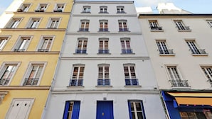 Un immeuble à plusieurs étages doté d’une porte bleue au centre, de façades blanches et jaunes, et de balcons avec des garde-corps noirs.