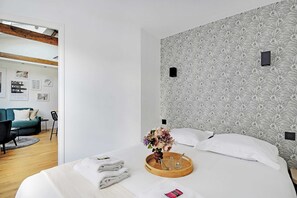 A modern hotel room with a large bed, a wooden tray with towels and a vase of flowers, a patterned wall, and a view of the adjacent living area. - Magnific location - 1BDR/4P - Gare de Lyon (Paris)