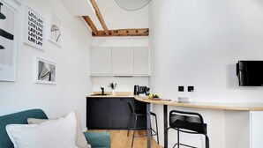 Cocina compacta con techo de madera, zona de comedor con taburete de bar y sofá con cojines.