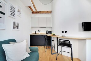 Eine kompakte Küche mit Holzboden, eine Essecke mit Barhocker und eine Couch mit Kissen.