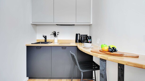 Una cocina compacta con un mueble gris, una encimera de madera, una silla negra y un frutero con manzanas y un pimiento.