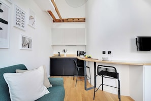 Een compacte keuken met een houten plafond, een zithoek met een barstoel en een bank met kussens.