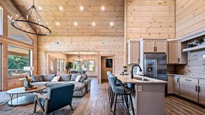 A spacious living area with a large sofa, a coffee table, and a kitchen area with a stainless steel refrigerator and wooden cabinets.