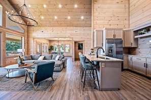A spacious living area with a large sofa, a coffee table, and a kitchen area with a stainless steel refrigerator and wooden cabinets.