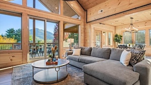 A spacious living room with a large gray sectional sofa, a round coffee table, and a dining area with a chandelier.