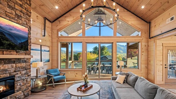 A spacious living room with a stone fireplace, a large sofa, a round coffee table, and a chandelier.