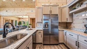 A modern kitchen with a stainless steel refrigerator, granite countertops, wooden cabinets, and a built-in sink.
