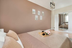 A bedroom with a large bed, a bedside table with a tray of items, and a wall with framed pictures.