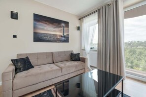 A modern living room with a beige sofa, a glass coffee table, and a painting of a lighthouse.