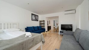 A modern hotel room with a bed, a blue sofa, a grey sofa, a TV, and a dining area. - Air-conditioned Studio for 6 Persons | 600 m from the Market Square (Wrocław)