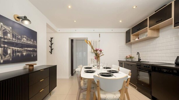 A modern kitchen with a dining table set for four, a black stove, and a white tiled backsplash. - Air-conditioned Studio for 6 Persons | 600 m from the Market Square (Wrocław)