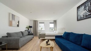A modern room with a grey sofa, a blue sofa, a small wooden table, and a bed with a view. - Air-conditioned Studio for 6 Persons | 600 m from the Market Square (Wrocław)