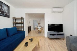 A modern living room with a sofa, TV, coffee table, and a dining area in the background.