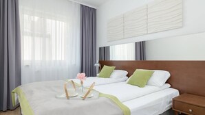 A hotel room with two beds, a wooden nightstand, and a large window with curtains.