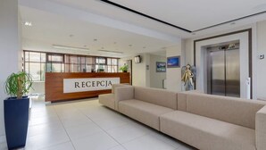 A reception area with a reception desk labeled "RECEPCJA," a beige sofa, a potted plant, and an elevator.