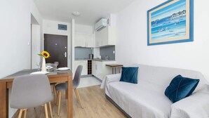 A modern, well-lit room with a dining area, kitchenette, and a large bed with blue pillows.
