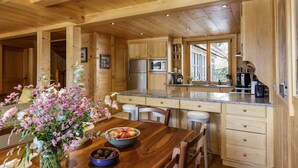 A wooden interior with a kitchen area, wooden cabinets, a dining table with chairs, and a vase of flowers. - Chalet Scierie - luxury chalet with hot tub (Chamonix-Mont-Blanc)