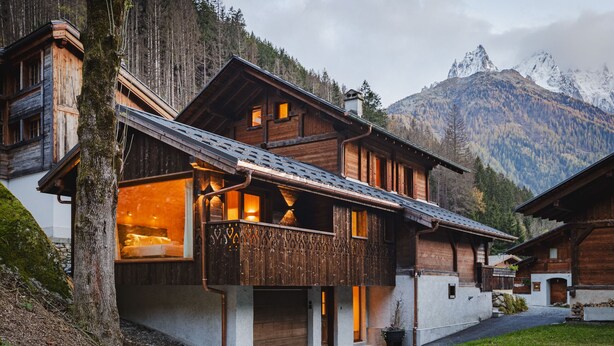 A wooden chalet with a balcony, large windows, and a garage. It is surrounded by a mountainous landscape. - Chalet Scierie - luxury chalet with hot tub (Chamonix-Mont-Blanc)