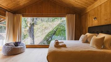 Camera da letto in una baita di legno con un'ampia finestra, un letto e una poltrona sacco.