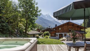 A wooden deck with a hot tub, a table with chairs, and a mountain view. - Chalet Scierie - luxury chalet with hot tub (Chamonix-Mont-Blanc)