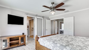 Ein Schlafzimmer mit einem Bett, einem Holzschrank, einem Deckenventilator und einem Fernseher an der Wand.