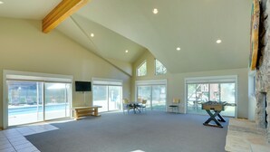 Una habitación amplia con techo alto, ventanas grandes, chimenea de piedra y vistas a la piscina.