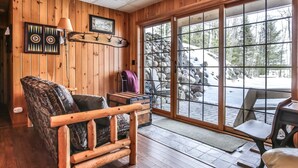 Un interior de madera con un amplio ventanal corredera que da a un espacio exterior con rocas y árboles.