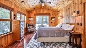 Un dormitorio tipo cabaña acogedor, con una cama grande, cómoda y silla, paredes de madera y ventana con vistas a un paisaje nevado.