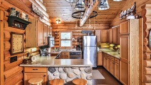 Cocina de cabaña de madera con una isla central, armarios de madera, una pared decorativa de piedra y una lámpara colgante.