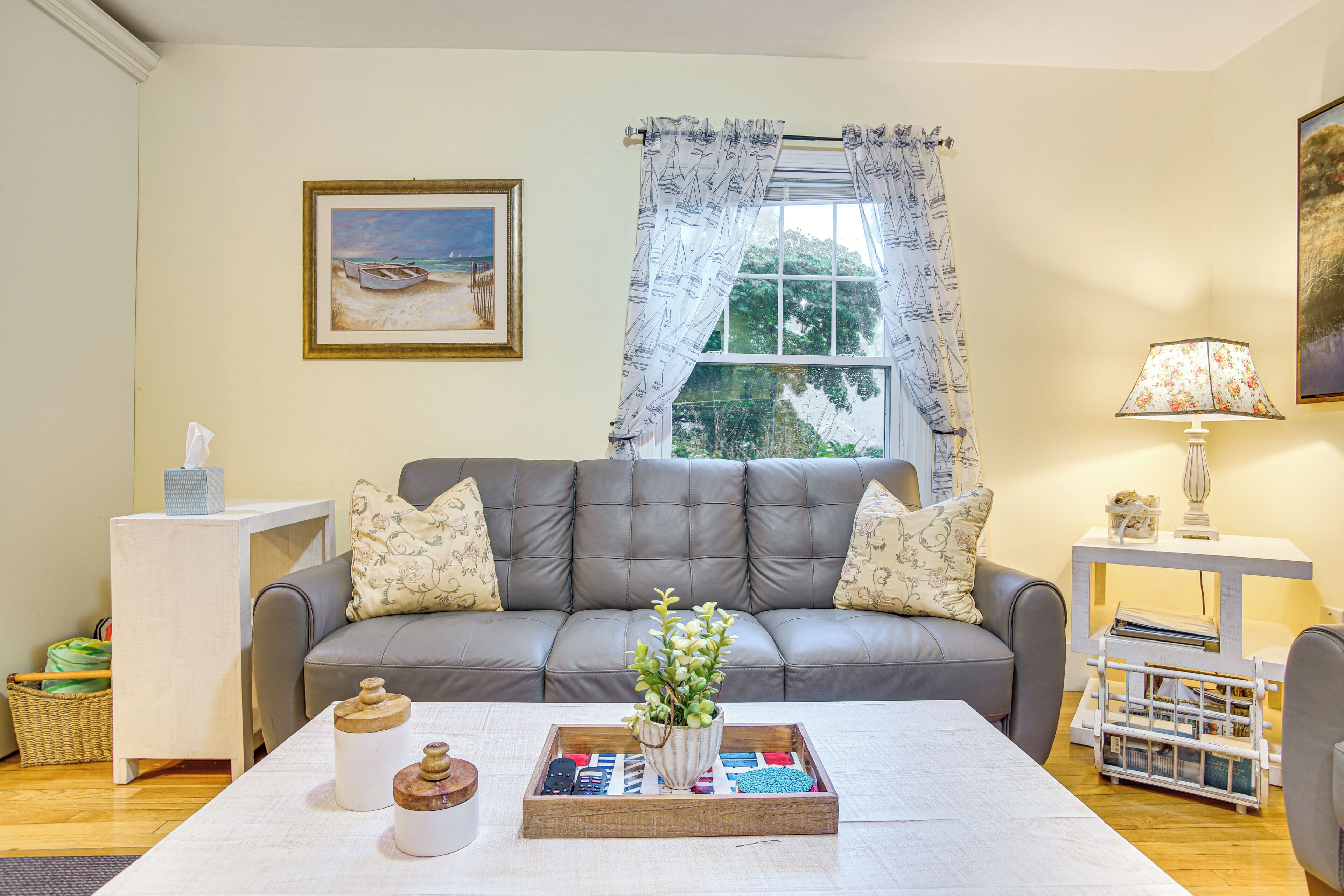 A living room with a grey sofa, a coffee table with decorative items, a window with curtains, and a painting on the wall.