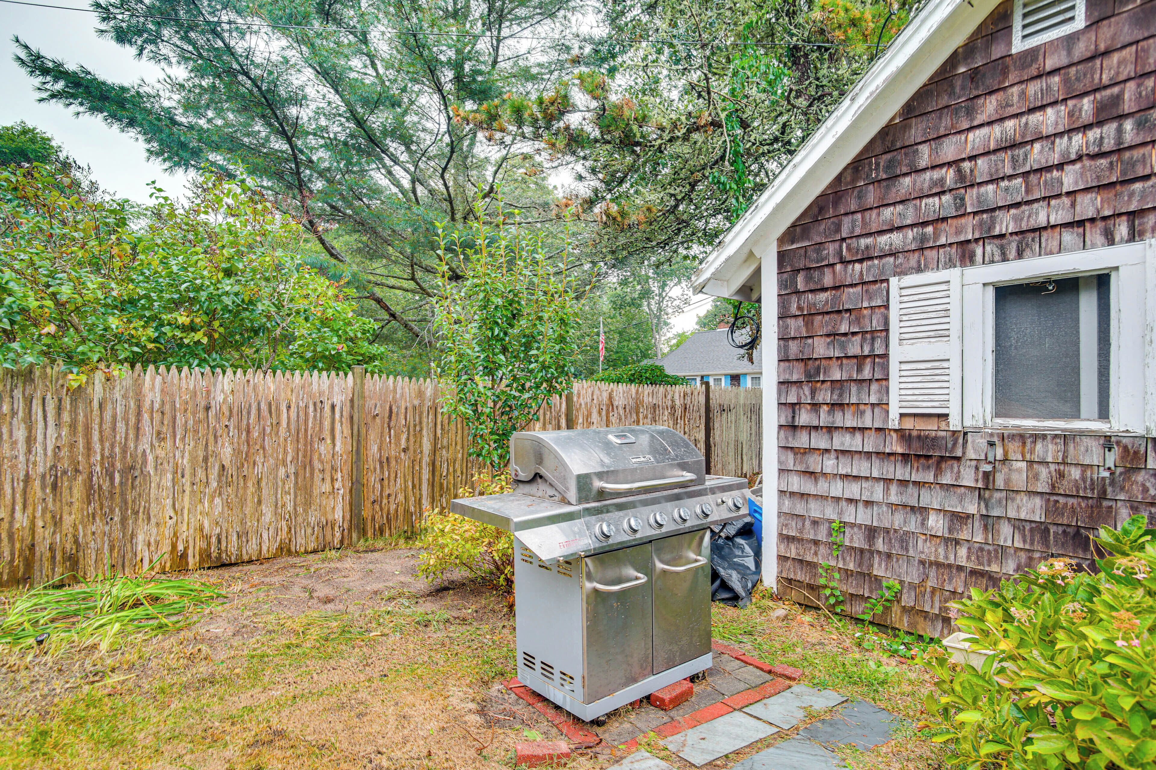 A backyard with a barbecue grill, wooden fence, and a house with a window.